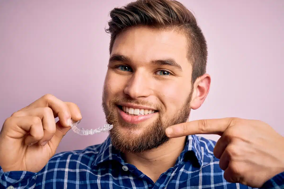 L'homme tient un appareil dentaire invisible dans sa main et le montre du doigt.