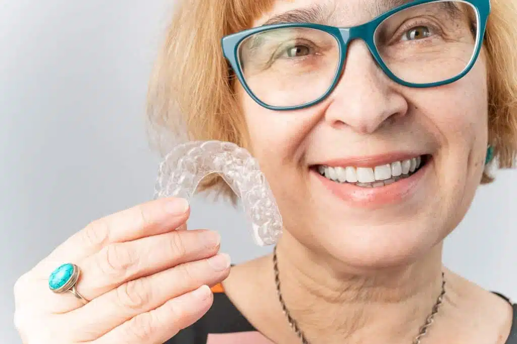 Older woman holds her DrSmile retainer in her hand and smiles