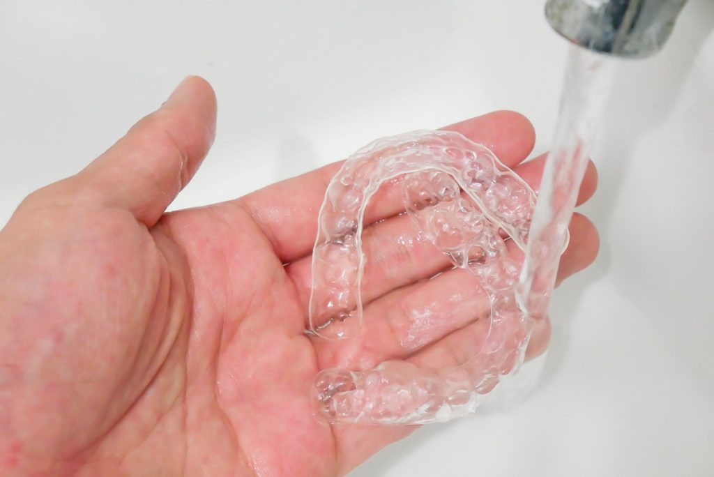 Zahnschiene reinigen: Aligner werden mit Wasser abgespült