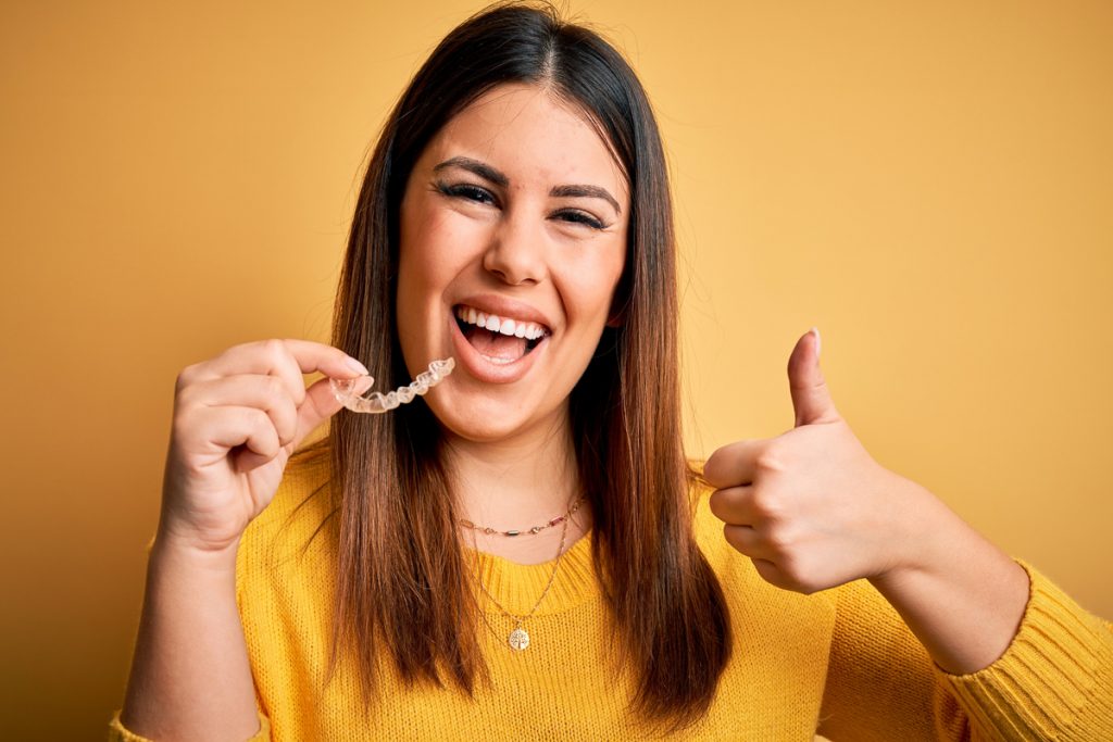 En kvinna håller en tandställning i handen och ler med tummen upp.