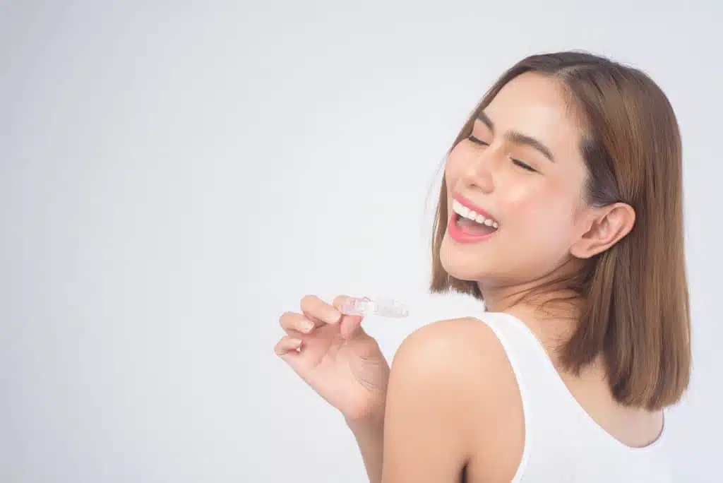 Woman holds aligner in hand and smiles