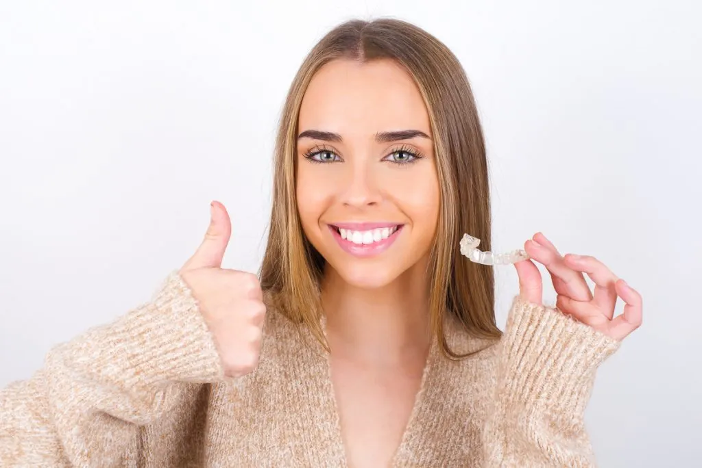 Ung kvinna som håller en tandställning med ett leende - Braceless Experiences