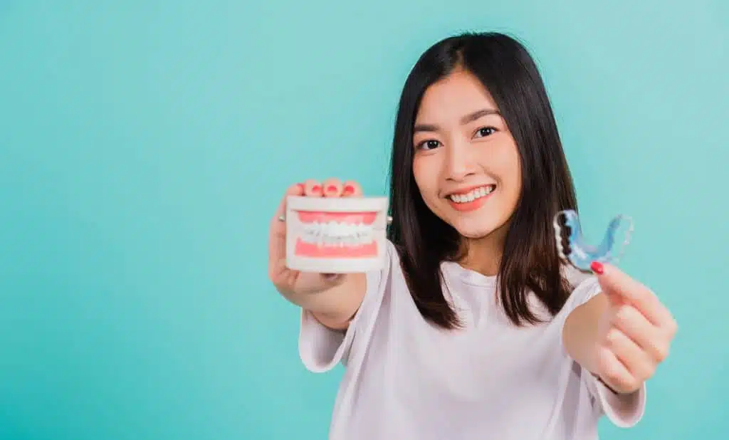 Young woman smiling holds denture and aligner in camera