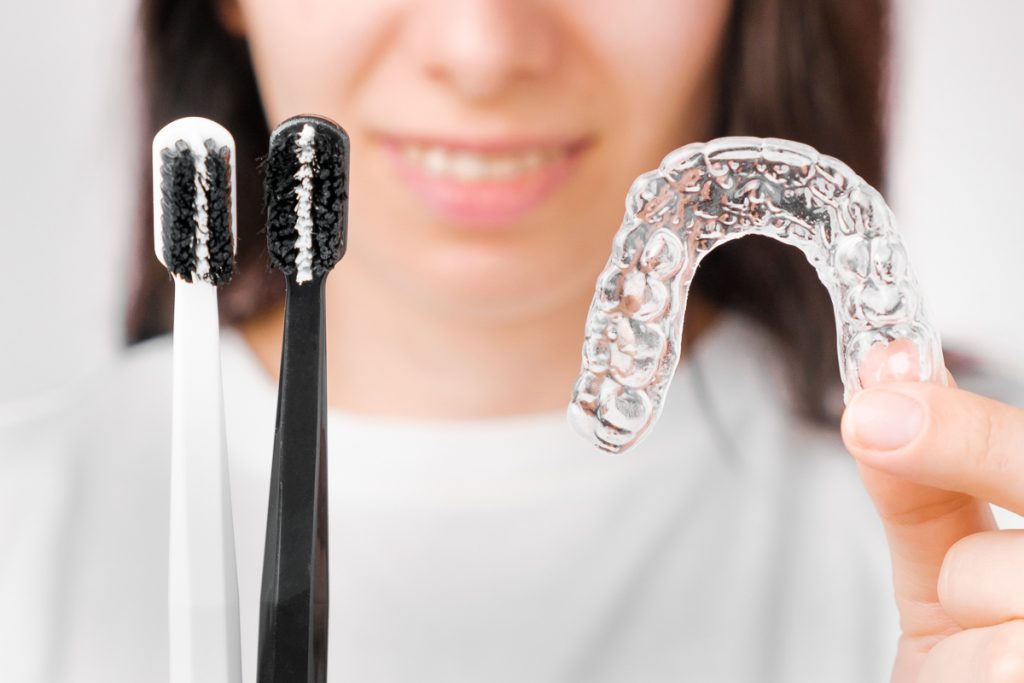 Limpieza alineador alineador: Mujer joven limpia el alineador con un cepillo de dientes