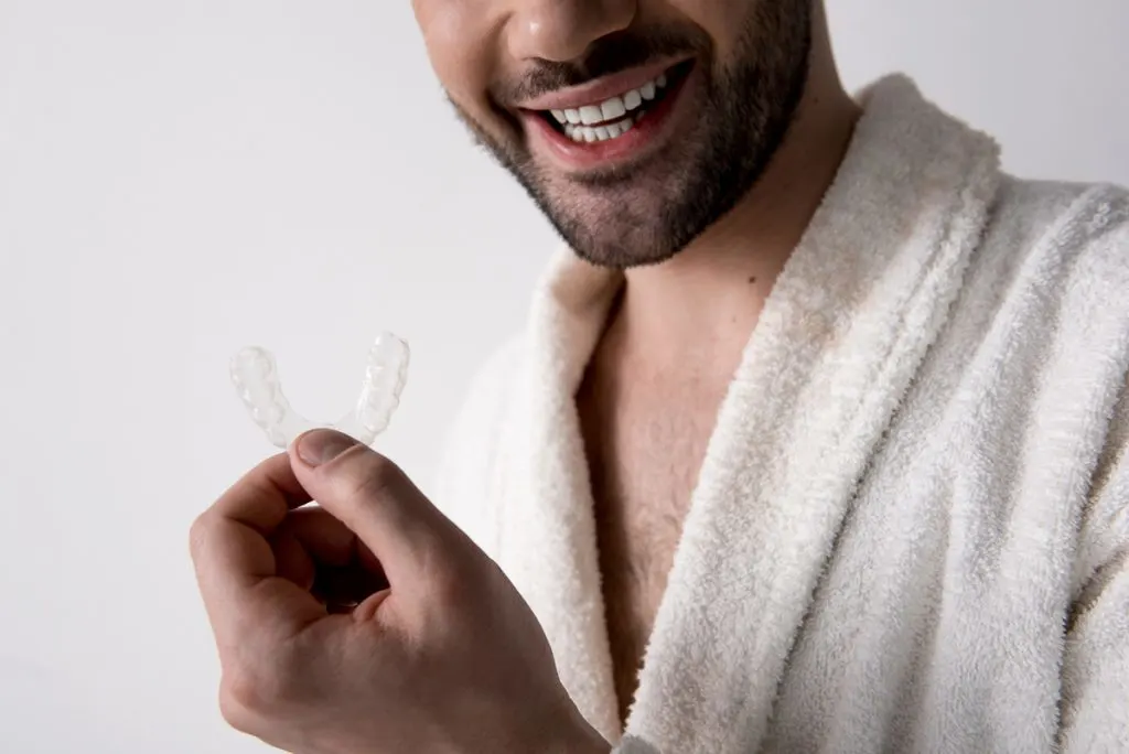 Jonge man glimlacht en houdt onzichtbare tandartsspalk in zijn hand