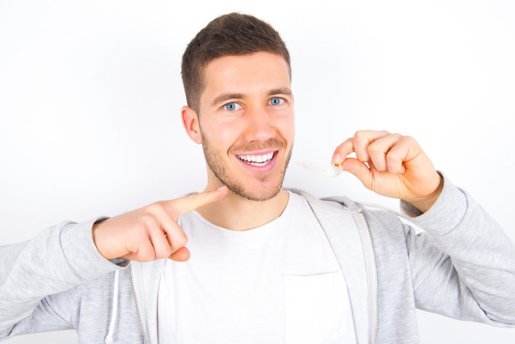 Młody mężczyzna uśmiecha się i trzyma w ręku niewidzialną szynę dentystyczną