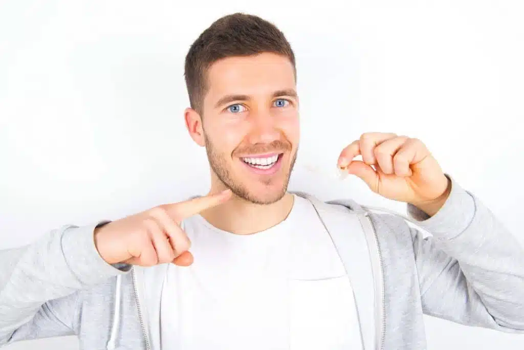 DrSmile prices - young man smiling holding invisible aligner in hand