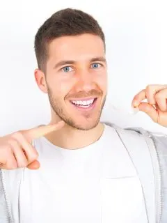 Junger Mann hält lächelnd unsichtbare Zahnschiene in der Hand