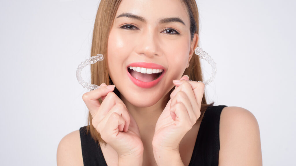 Woman smiling holding up aligner pair - dental insurance aligners