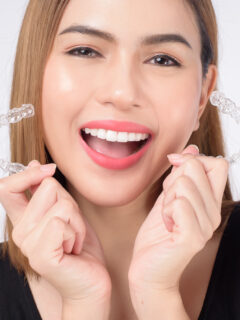 Frau hält lächelnd Aligner Paar nach oben - Zahnzusatzversicherung Aligner
