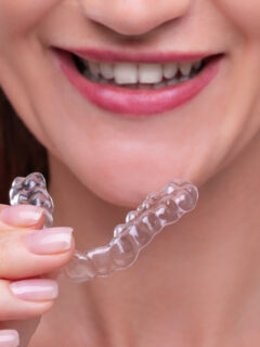 Woman is holding aligners in front of her face - nighttime clear aligners