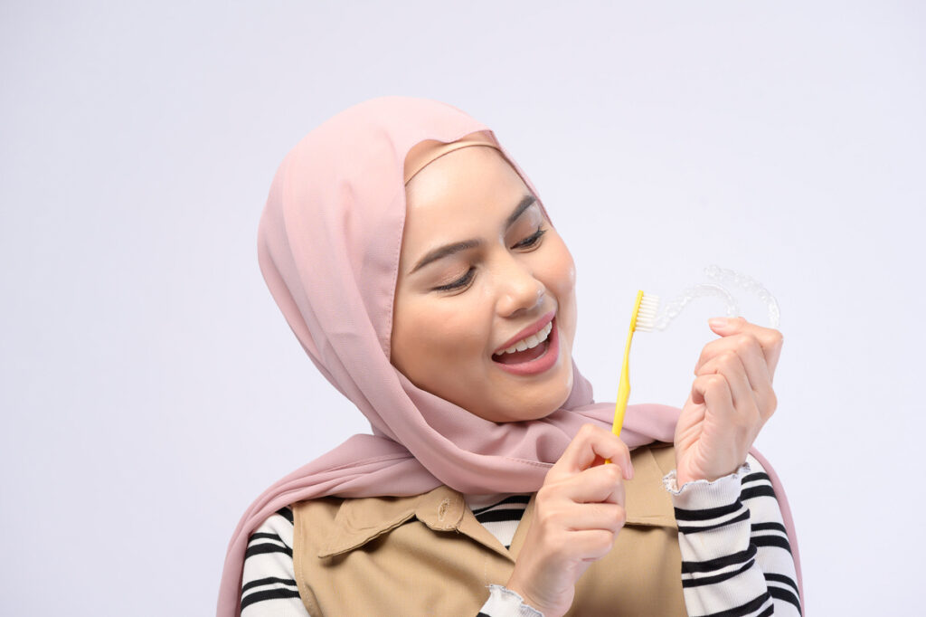 Young woman holding aligner and toothbrush - cleaning Invisalign 