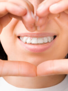 Lächelnde Frau formt mit ihren Händen Herz vor ihrem Gesicht - schiefe Zähne gerade machen